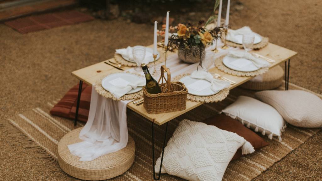 Boho-inspired low picnic table with candles, pillows, and neutral table decor set on a woven rug.