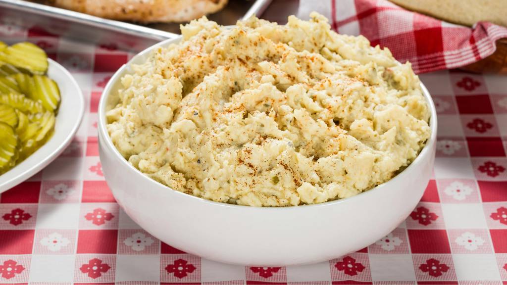 Bowl of potato salad placed on a red patterned table cloth for picnic table during a picnic meal.