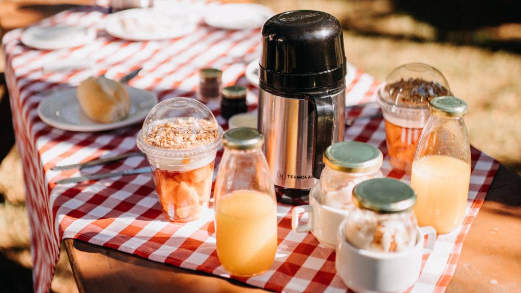 Outdoor breakfast setup with juice and coffee on a red gingham table cloth for picnic table.