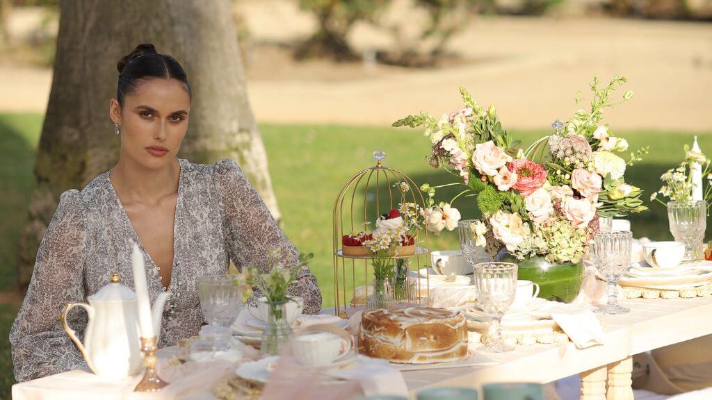 Elegant garden birthday picnic photoshoot Woman seated at an elegant outdoor picnic table decorated with flowers
