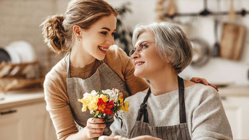 young woman giving flowers to mother-in-law in kitchen