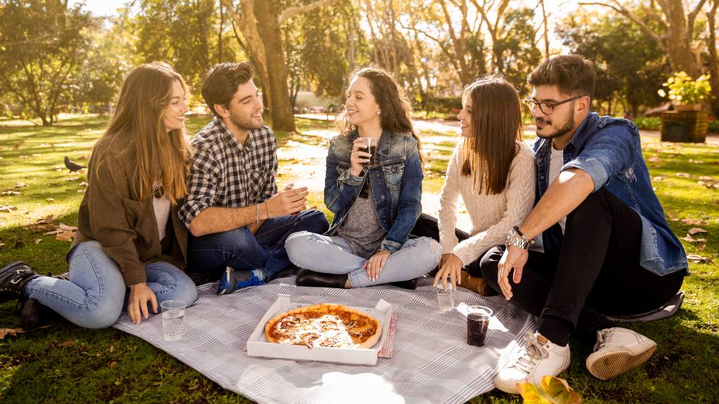 College picnic group enjoying pizza outdoors on a blanket