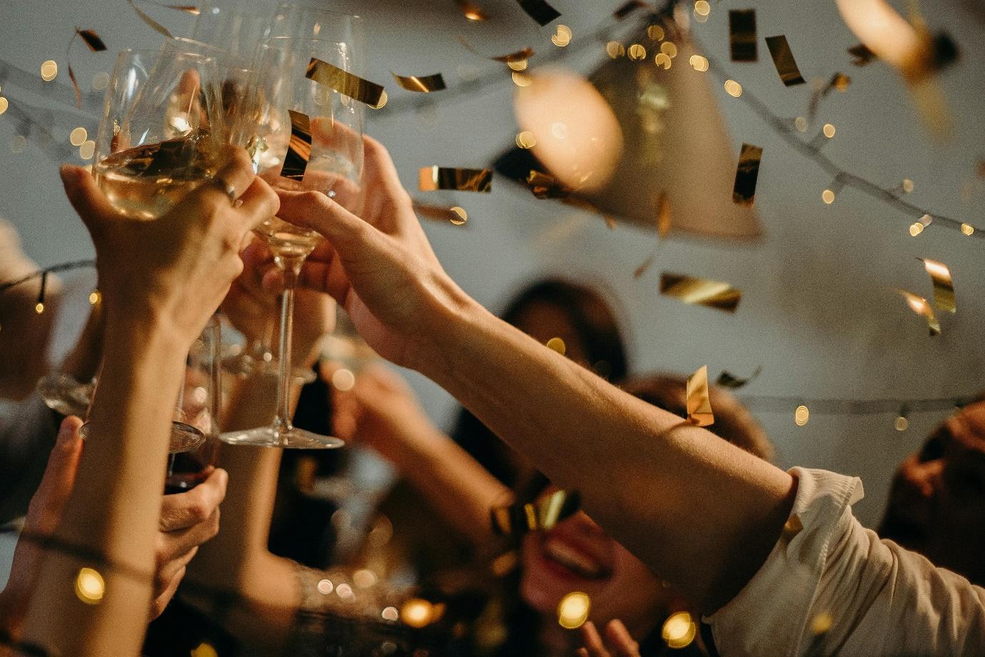 People raising glasses in a toast at a festive college party with confetti.