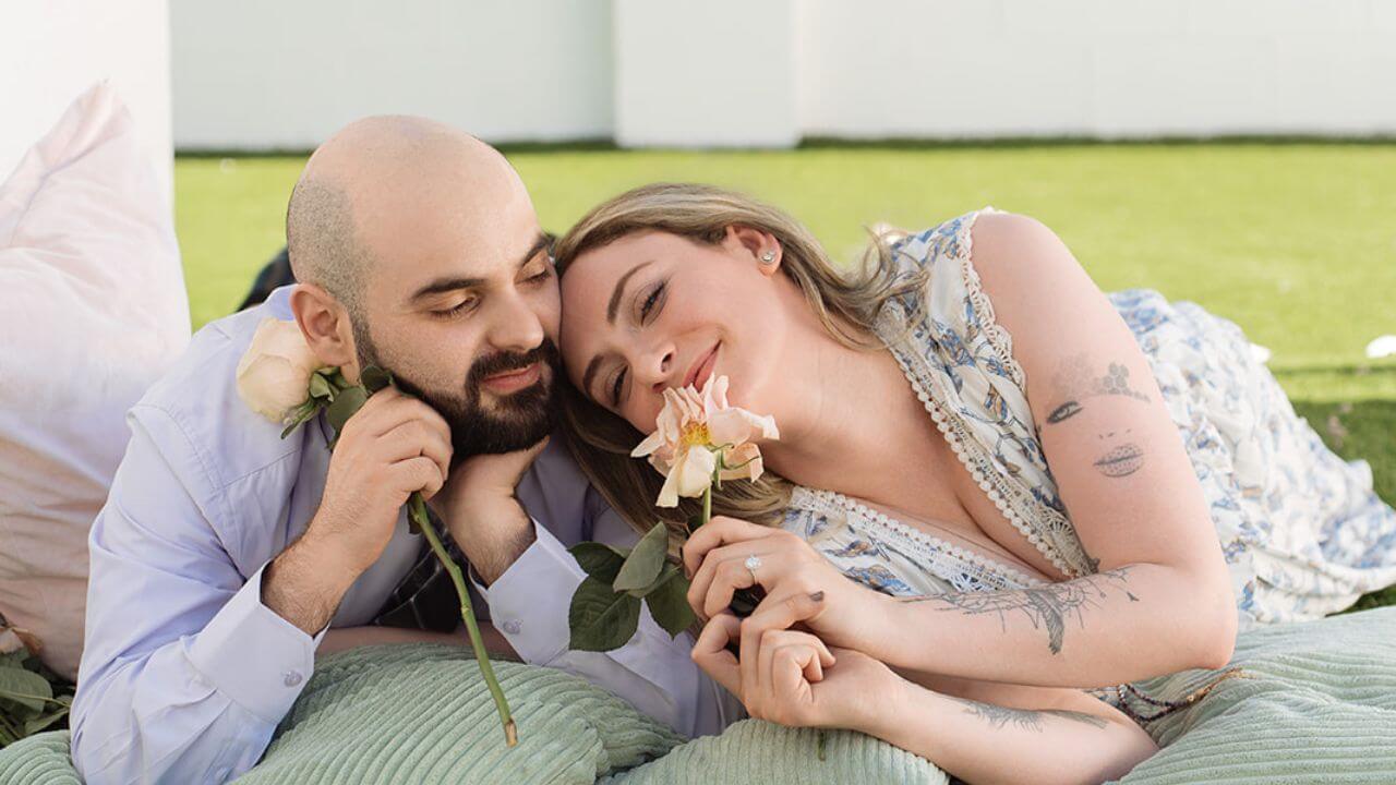 Couple relaxing together on soft cushions and holding pink roses during a romantic outdoor picnic