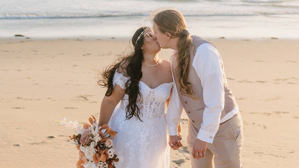 Newly married couple kissing by the ocean during their wedding day.