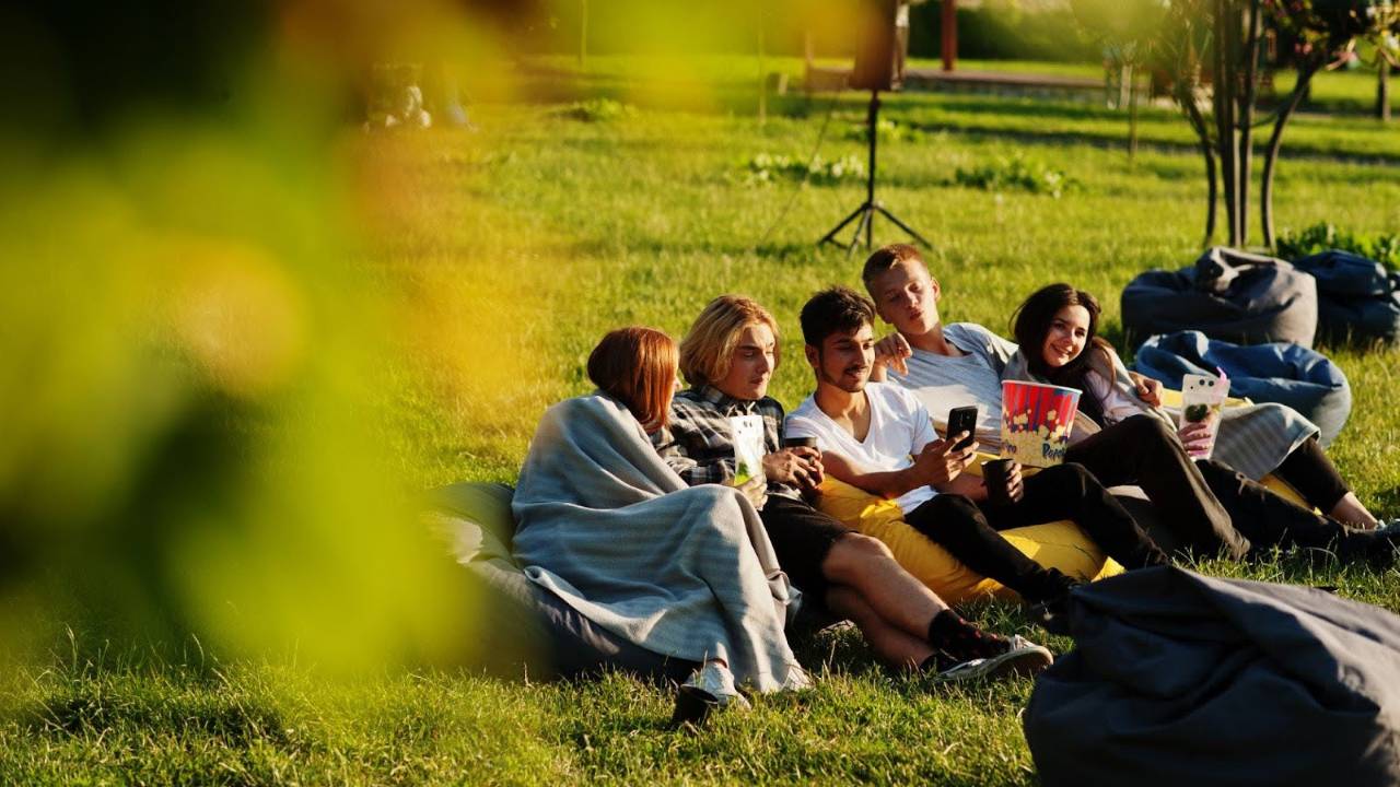 a group of students relaxing on bean bags outdoors, enjoying snacks and each other’s company after exams