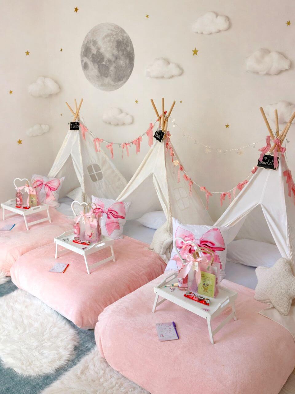 Pink moon and stars sleepover party setup with white teepees, pink bedding and personalized trays