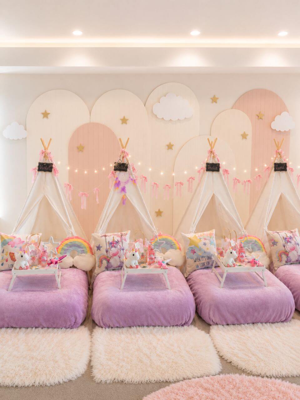 Unicorn themed sleepover party setup with white teepees, pink bedding and personalized decor